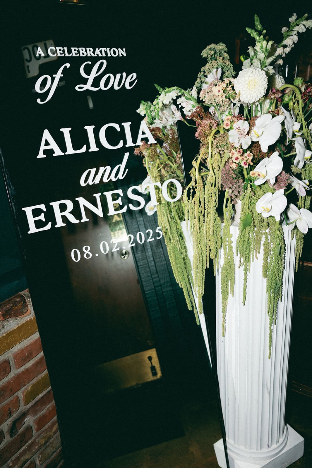 Photo of wedding signage and florals. Signage says "A celebration of Love. Alicia and Ernesto".